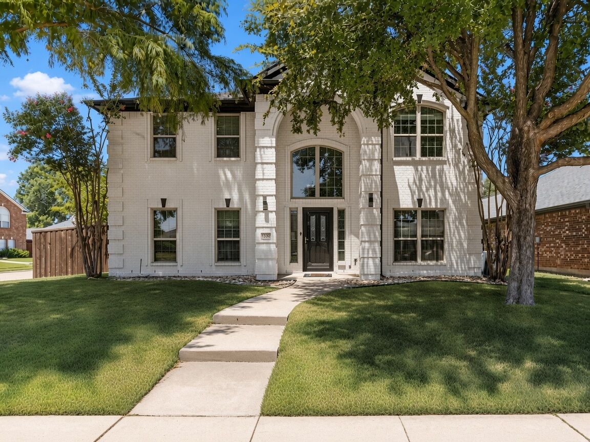 Two-story painted white brick home with an arched entry, black front door and mature shade trees